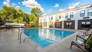 A swimming pool with a 3ft no diving sign, surrounded by lounge chairs and umbrellas, with a building in the background.