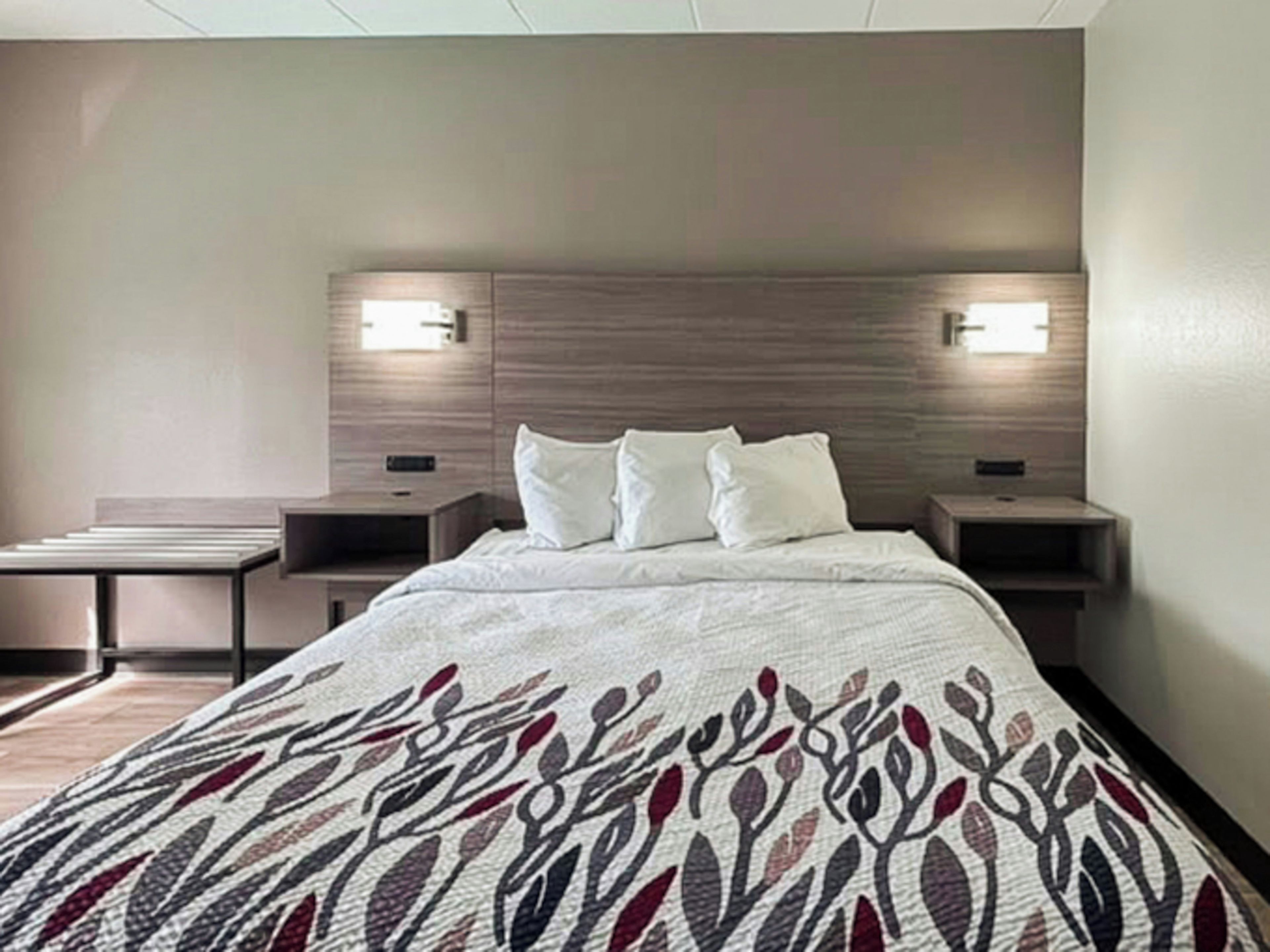 A hotel room with a bed, two bedside tables, and two wall-mounted lamps.