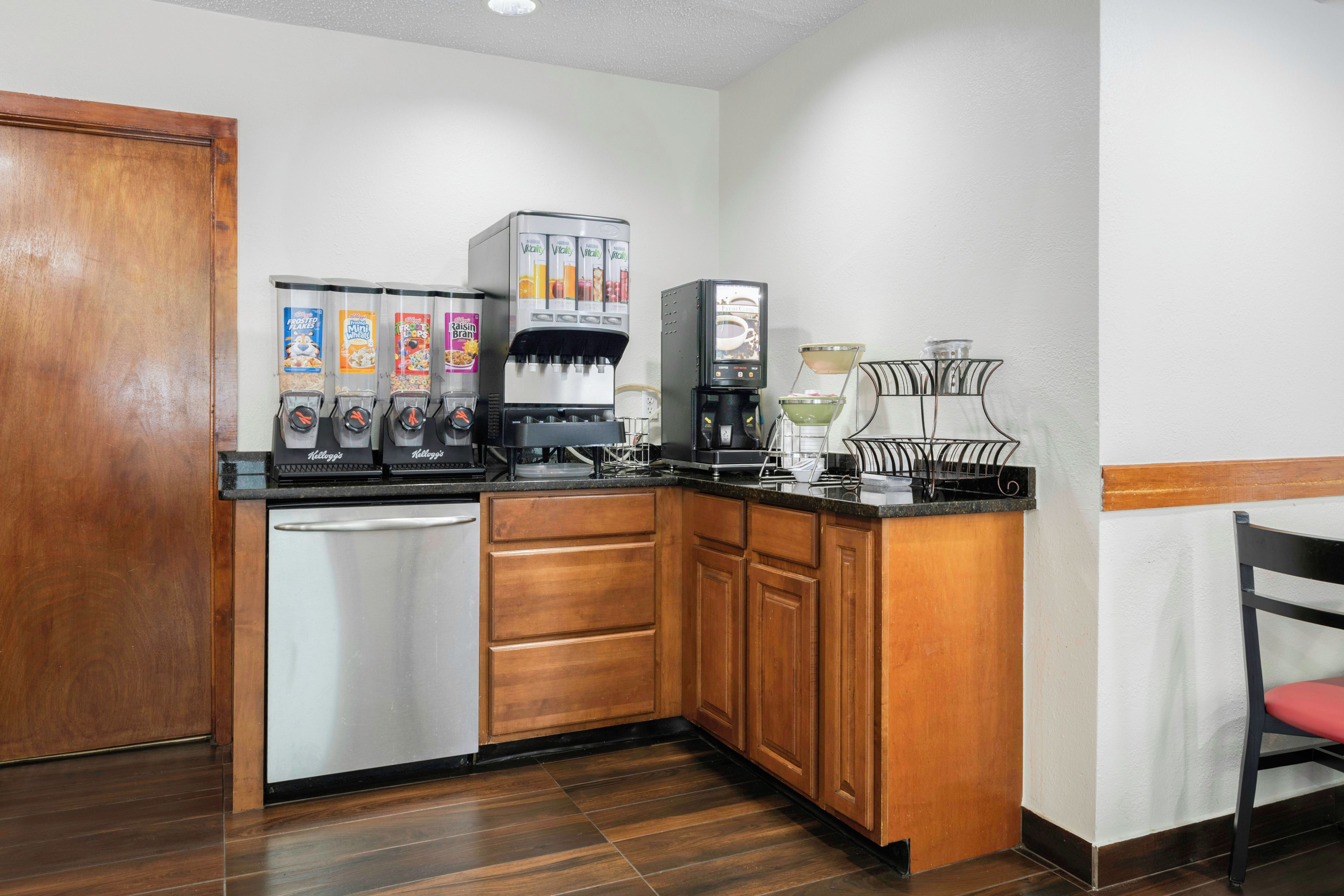 A compact kitchen with a dishwasher, wooden cabinets, a coffee machine, and a cereal dispenser.