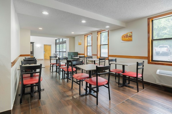 A clean, modern dining area with wooden flooring, red chairs, and white tables.