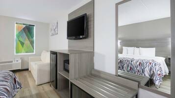 Une chambre d’hôtel comprenant un lit, un coin salon, une télévision et un grand miroir.