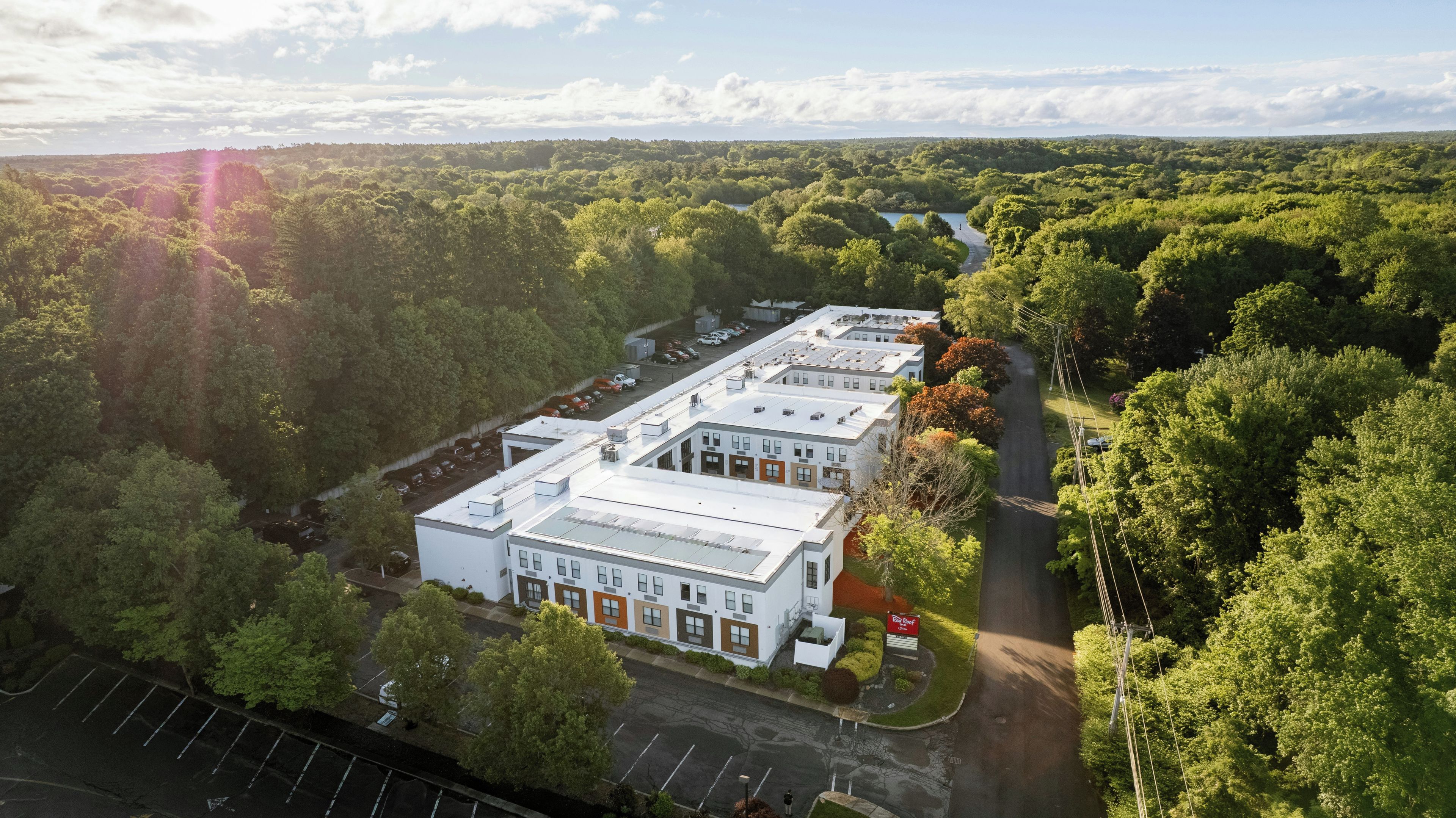 A multi-story building with a flat roof, surrounded by dense greenery and a clear sky.