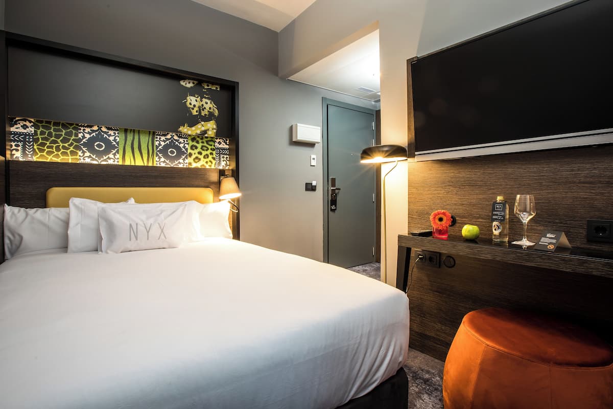 Una camera d'albergo con un letto grande, una scrivania con una lampada, una televisione e una porta.
