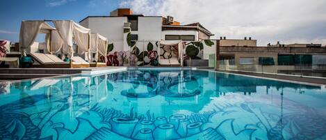 A rooftop pool with a clear blue water surface and a mural with the letters 'NYX' on the floor.