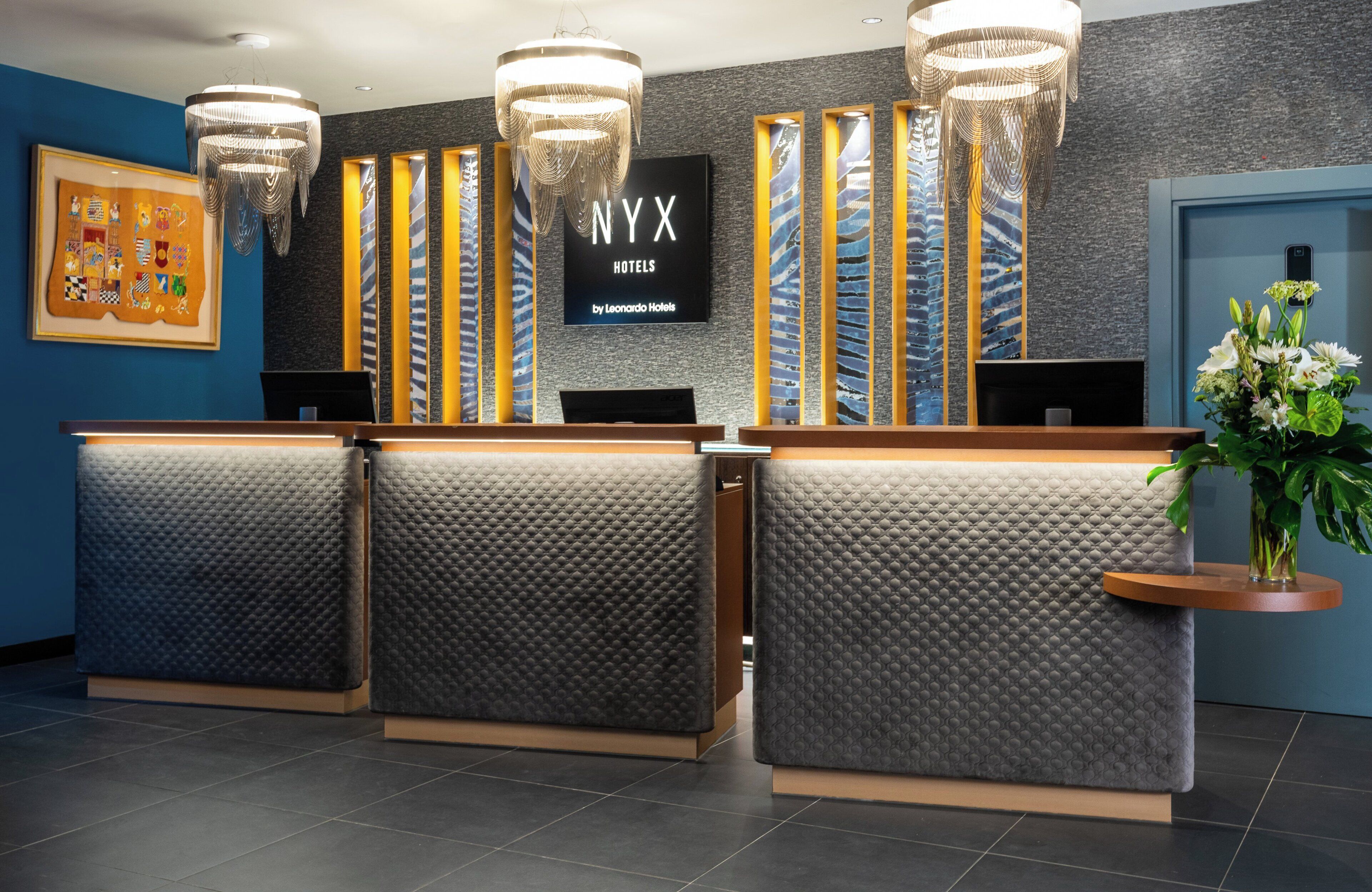 Un mostrador de recepción de hotel con diseño moderno, con un gran letrero de NYX Hotels by Leonardo Hotels.