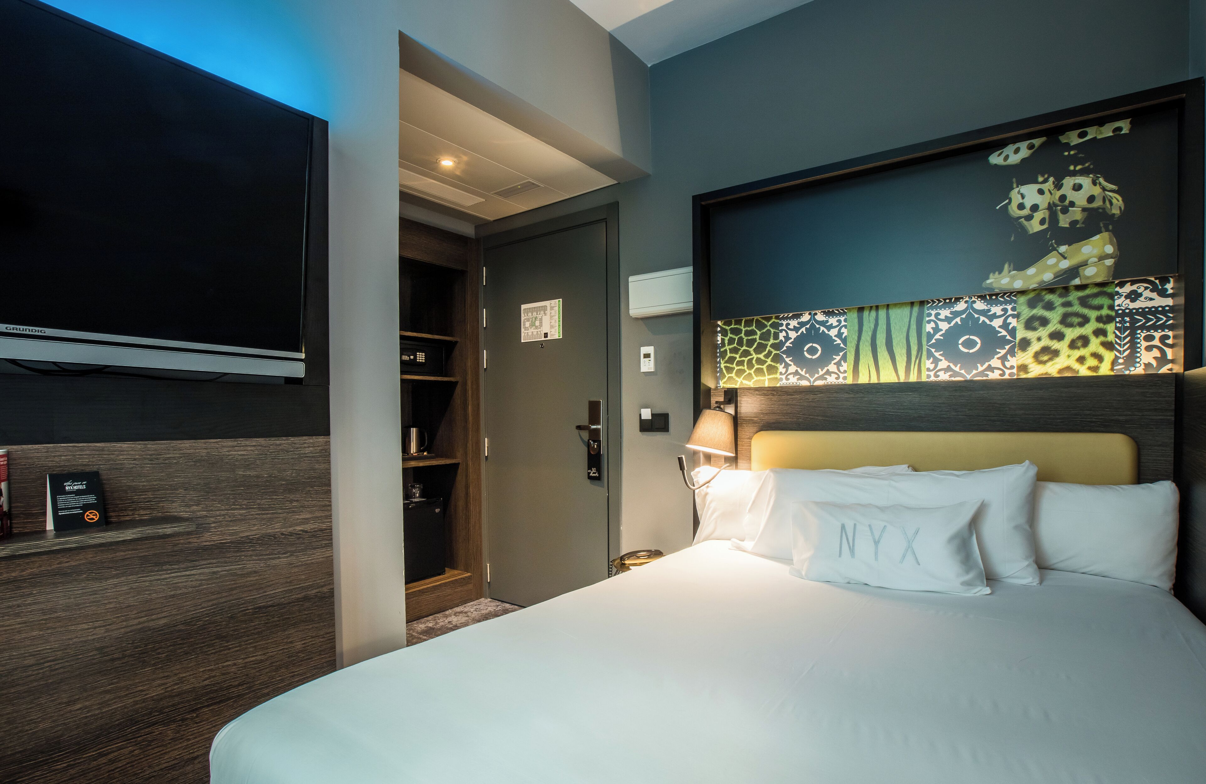 Une chambre d’hôtel avec un grand lit, un téléviseur fixé au mur, une armoire et une porte donnant sur une salle de bain.