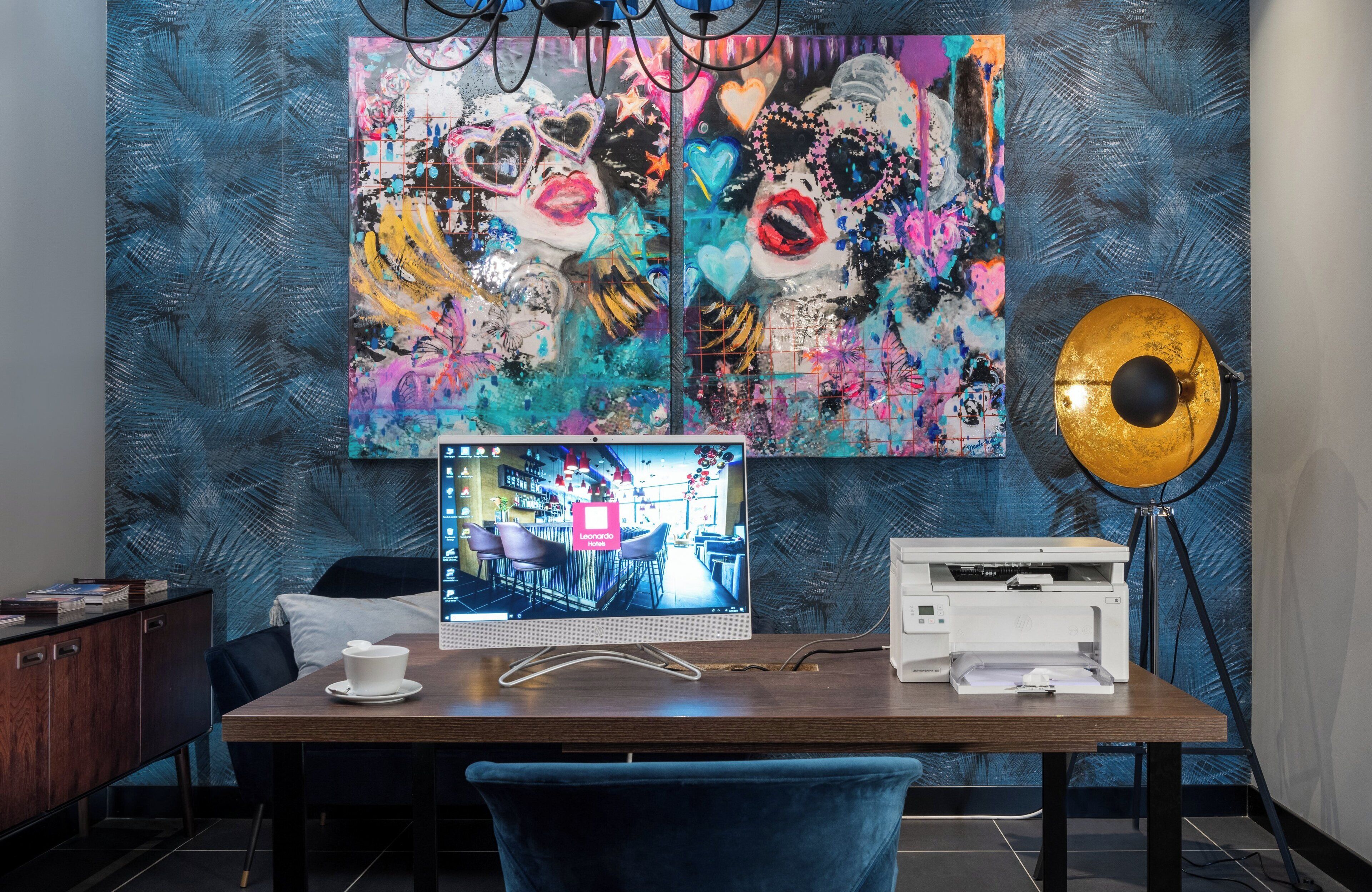 Habitación de hotel moderna con un cuadro abstracto grande en la pared, un escritorio con computadora, impresora y lámpara.
