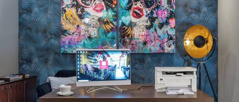 Habitación de hotel moderna con un cuadro abstracto grande en la pared, un escritorio con computadora, impresora y lámpara.