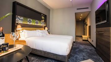 Una habitación de hotel moderna con una cama grande, lámparas de noche, una mesita con una botella de vino y una copa, y un cabecero decorativo.