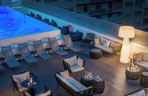 Un área de lounge en la azotea con disposición de asientos, una piscina y vistas del exterior del edificio.