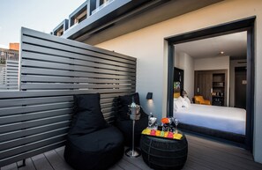 A modern outdoor seating area with a bench and a round table, a balcony with a view of the bedroom, and a bottle of champagne on the table. - NYX Hotel Madrid by Leonardo Hotels (Madrid)