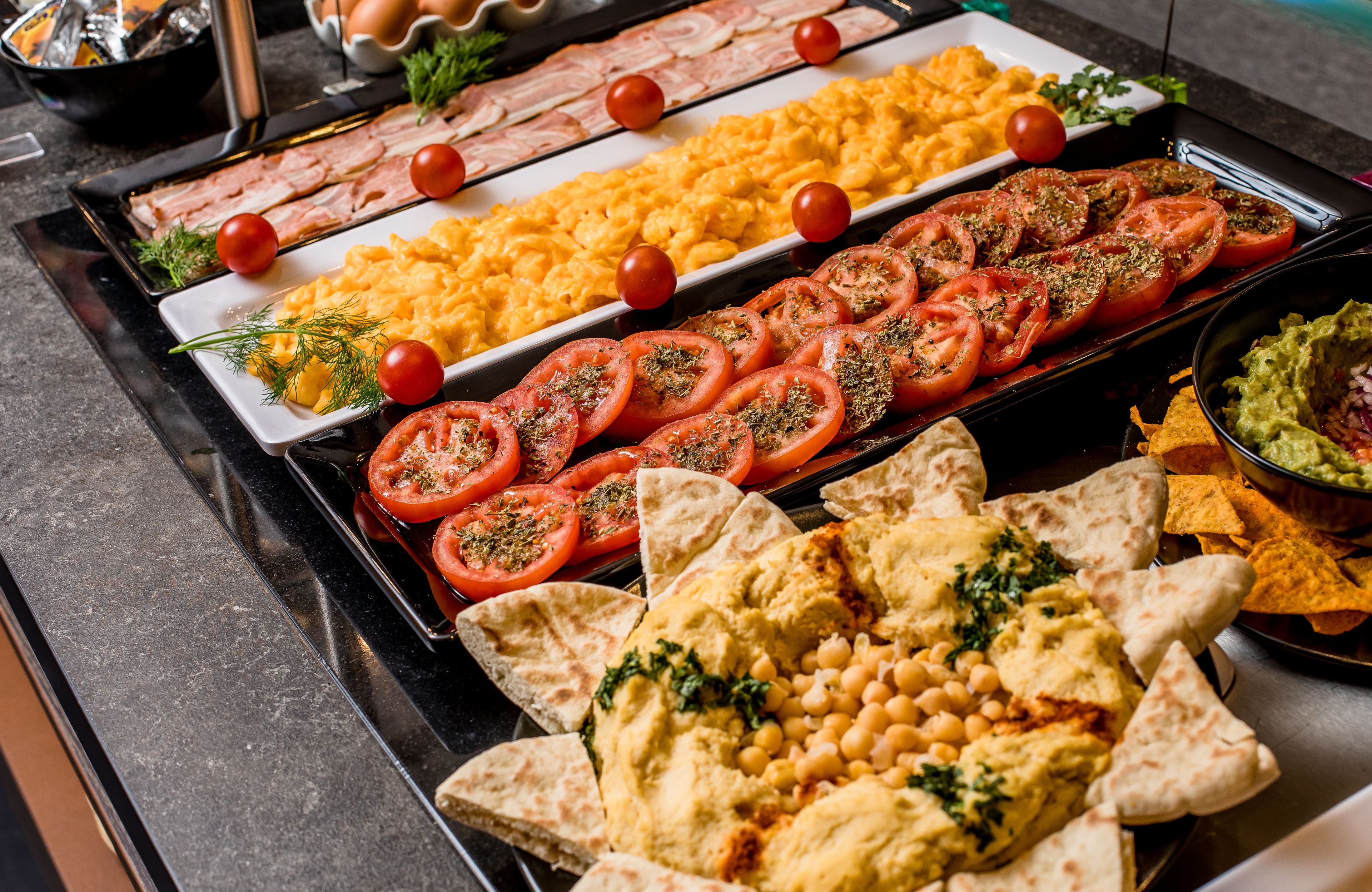 Un buffet con diversi piatti, tra cui uova strapazzate, pomodori e guacamole.
