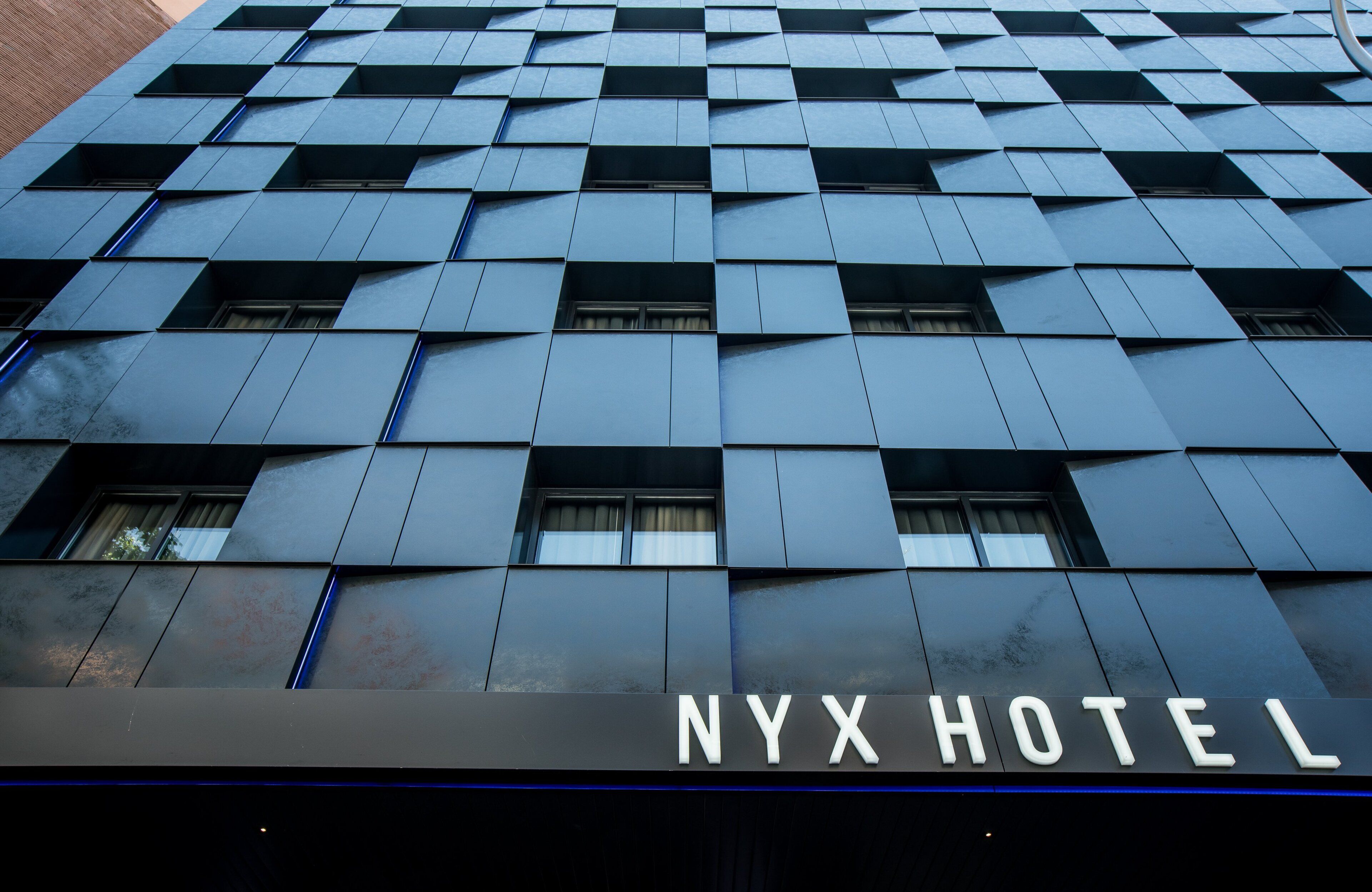 Exterior del hotel NYX, con una fachada moderna de diseño geométrico y señalización destacada.