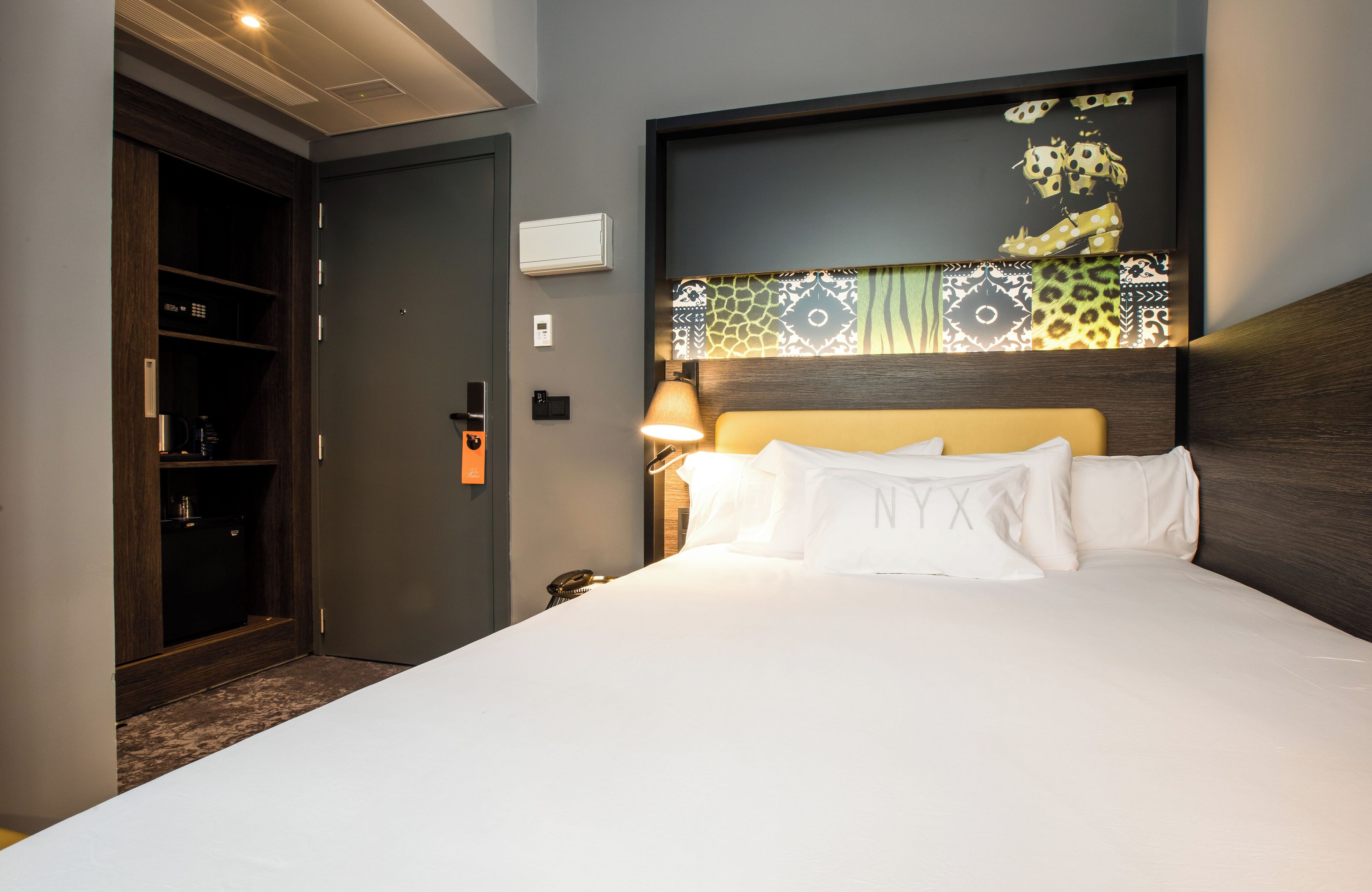 Una habitación de hotel con una cama, una mesita de noche, una lámpara, un armario y una puerta.