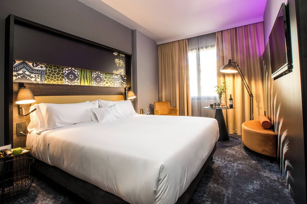 Una moderna camera d'albergo con un letto grande, due comodini, una sedia, una scrivania e una TV.