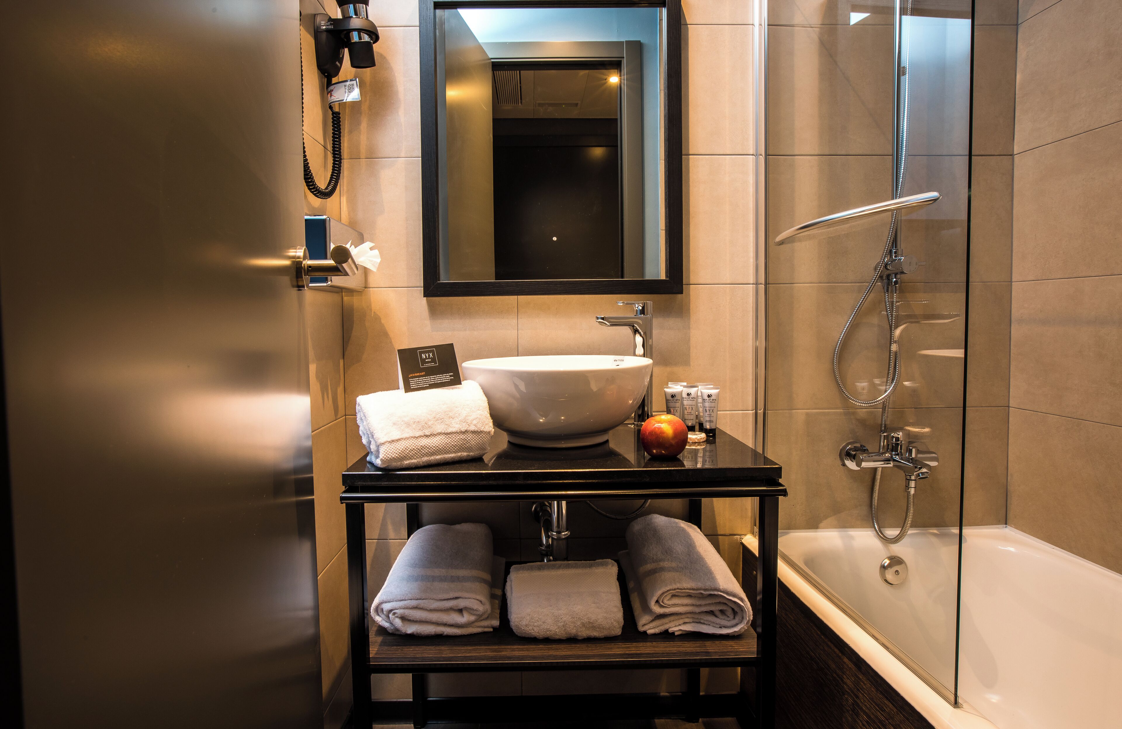 A modern bathroom with a large sink, a mirror, a glass-enclosed shower, and neatly folded towels on a shelf.