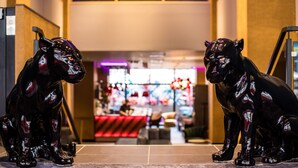 A lobby with two black cat statues, a staircase, and a bar area in the background.