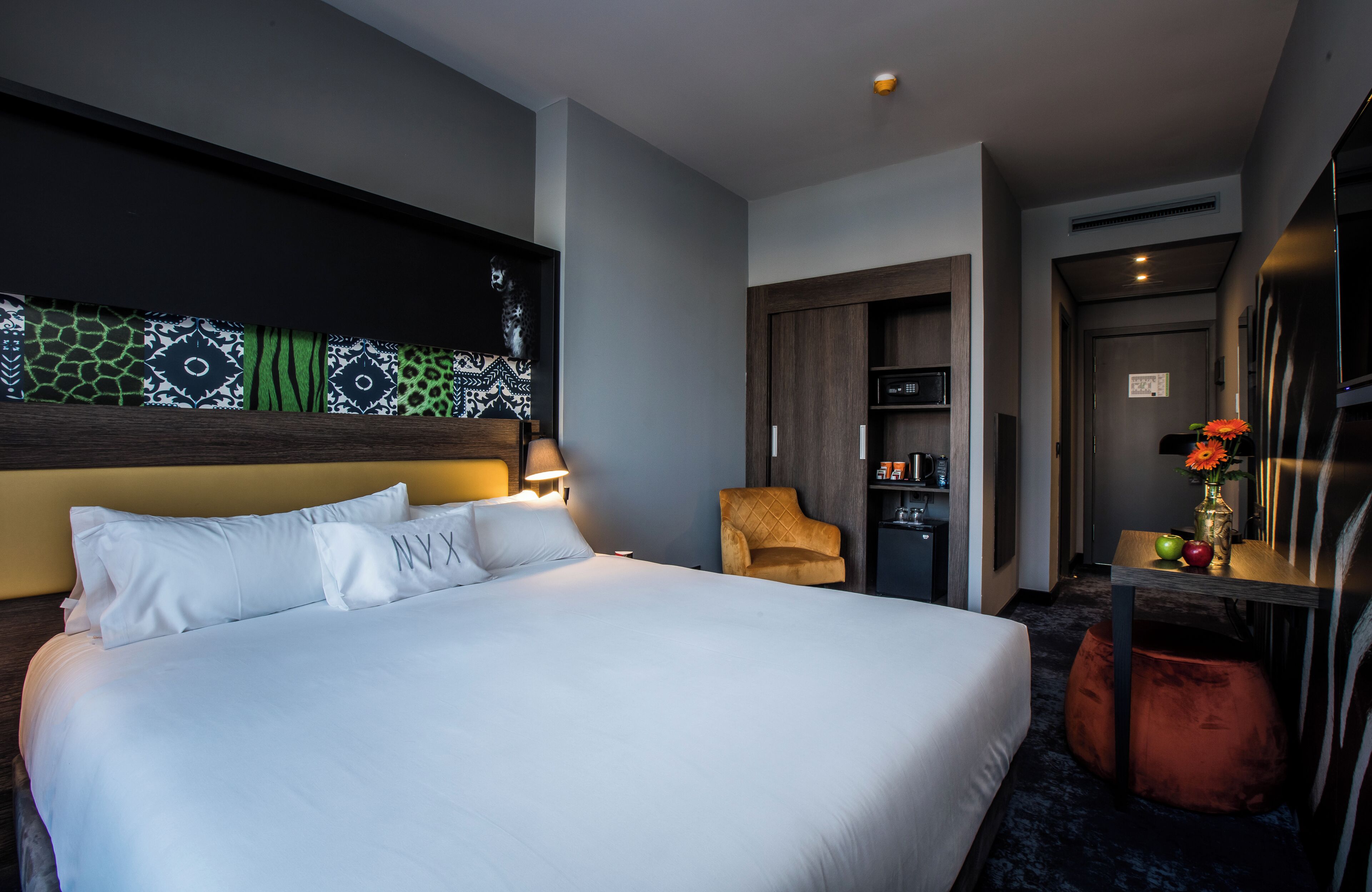 Una camera d'albergo moderna con un letto grande, una sedia, un tavolino con un vaso e un armadio.