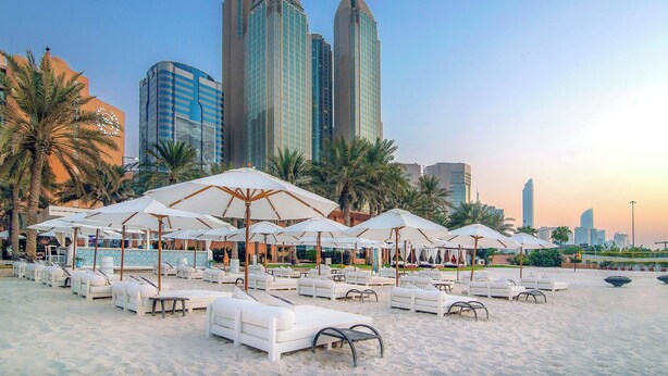 A beachside resort with lounge chairs and umbrellas, palm trees, and modern high-rise buildings in the background. - Sheraton Abu Dhabi Hotel & Resort (Abu Dhabi)