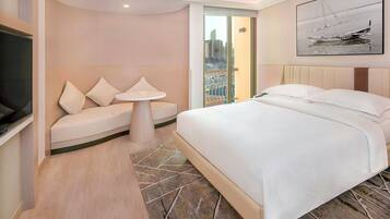 A hotel room with a bed, a sofa, a small table, and a view of the city through a glass door.