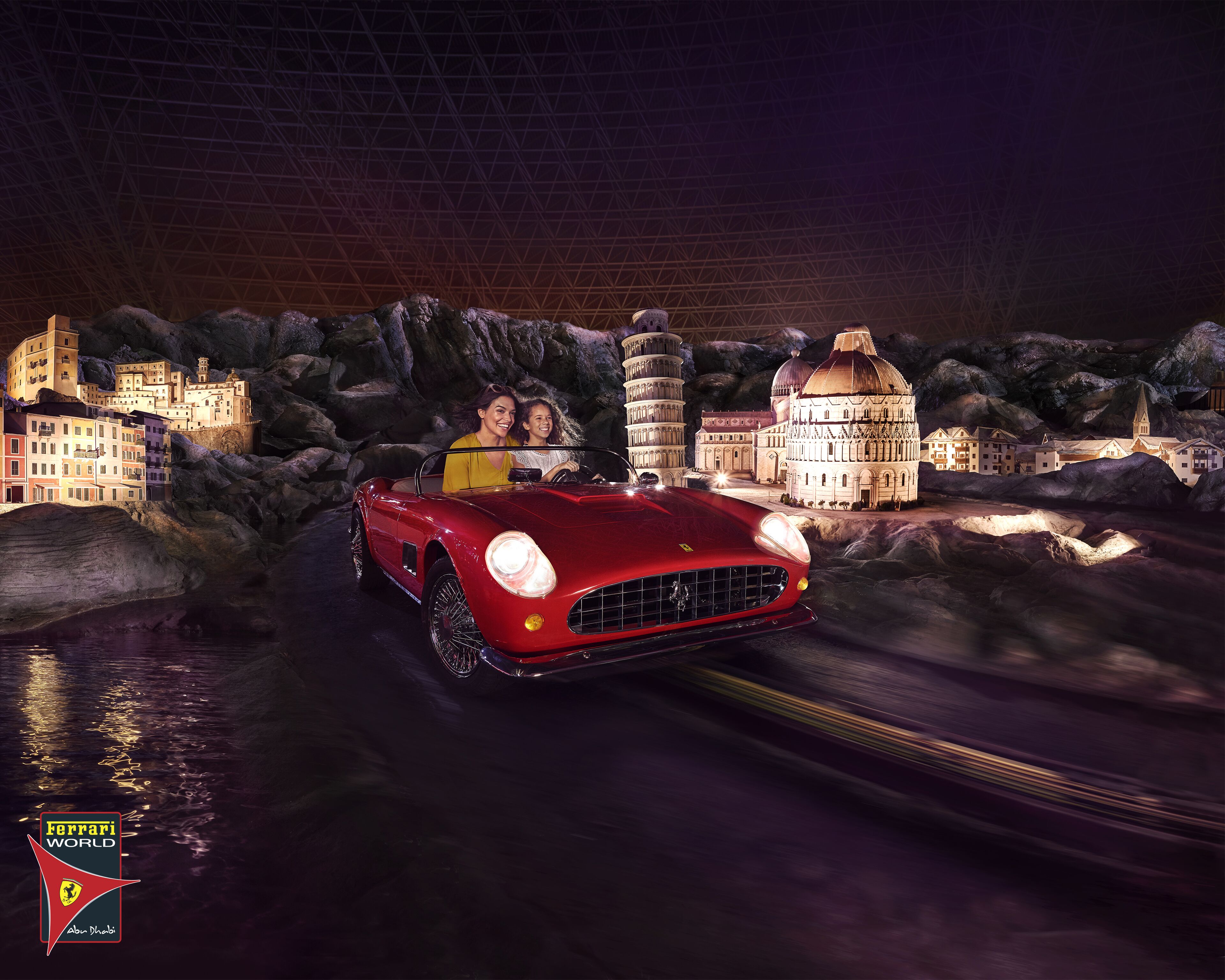 A red sports car driving on a road with a model of a cityscape in the background.