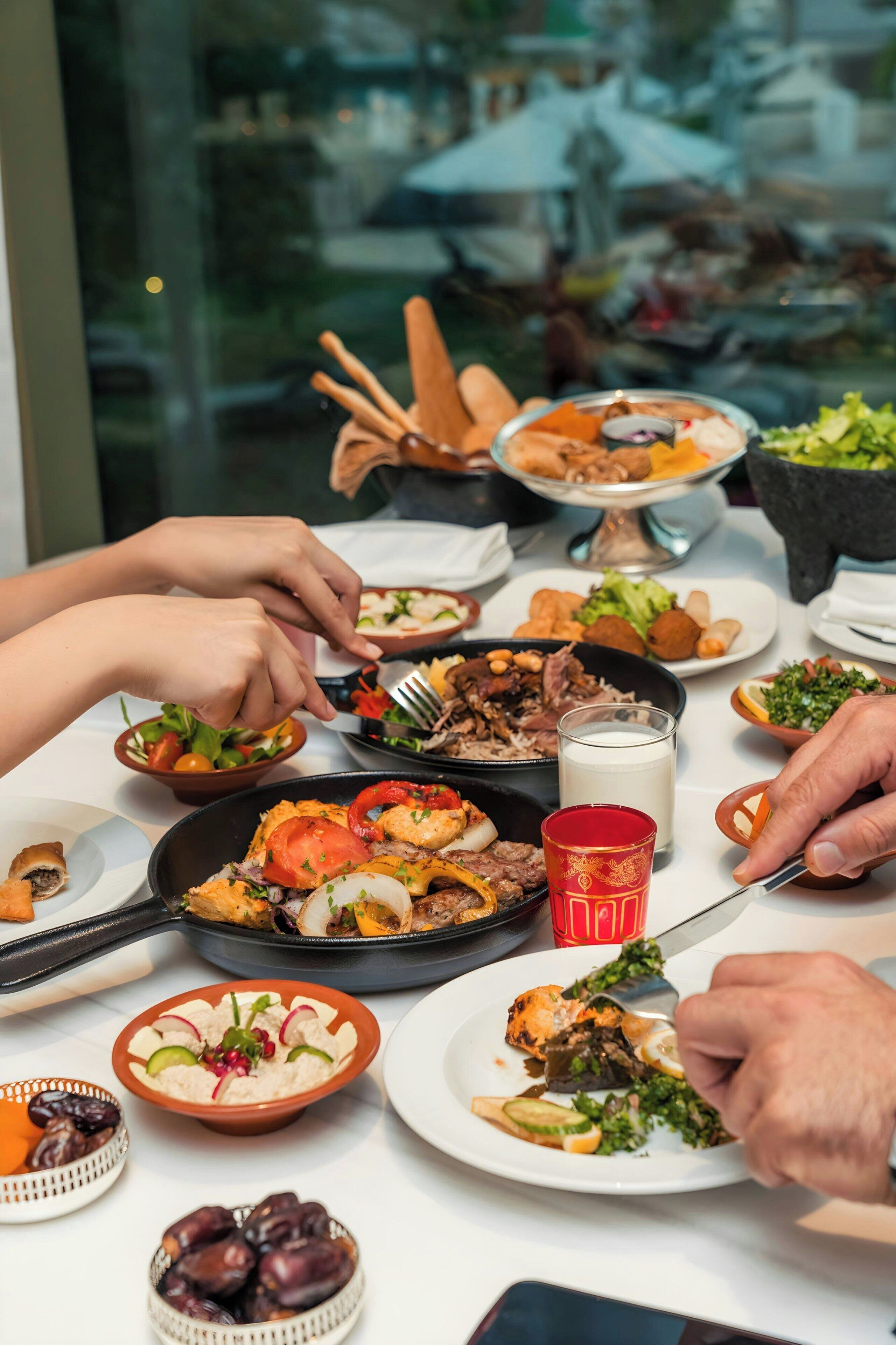 Una mesa con diversos platos, entre ellos una ensalada, carne en un plato y un cuenco de aceitunas.
