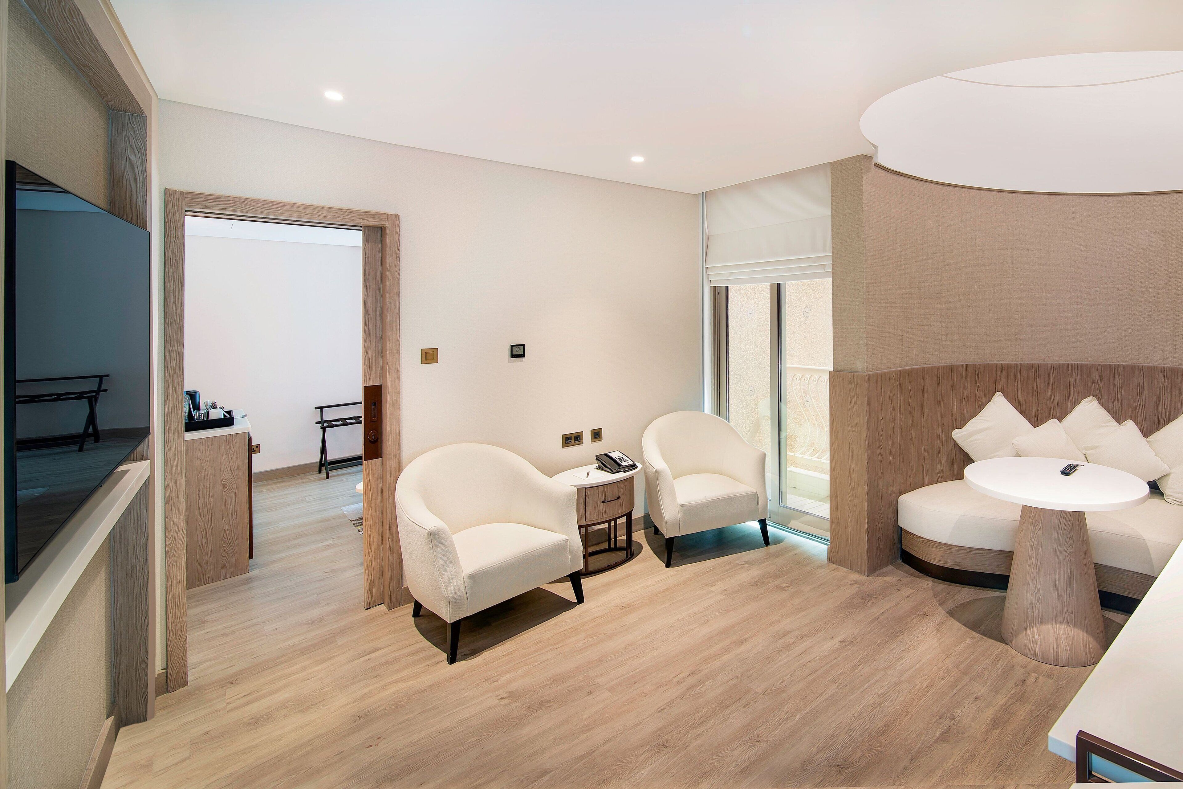 A modern hotel room with a sofa, two armchairs, a small table, and a wooden floor.