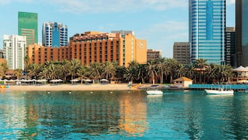 Un hôtel en bord de mer offrant une vue sur la plage, des palmiers et un port de plaisance avec des bateaux.