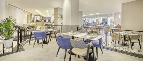 A spacious restaurant with multiple dining tables and chairs, a high ceiling with recessed lighting, and a modern interior design.