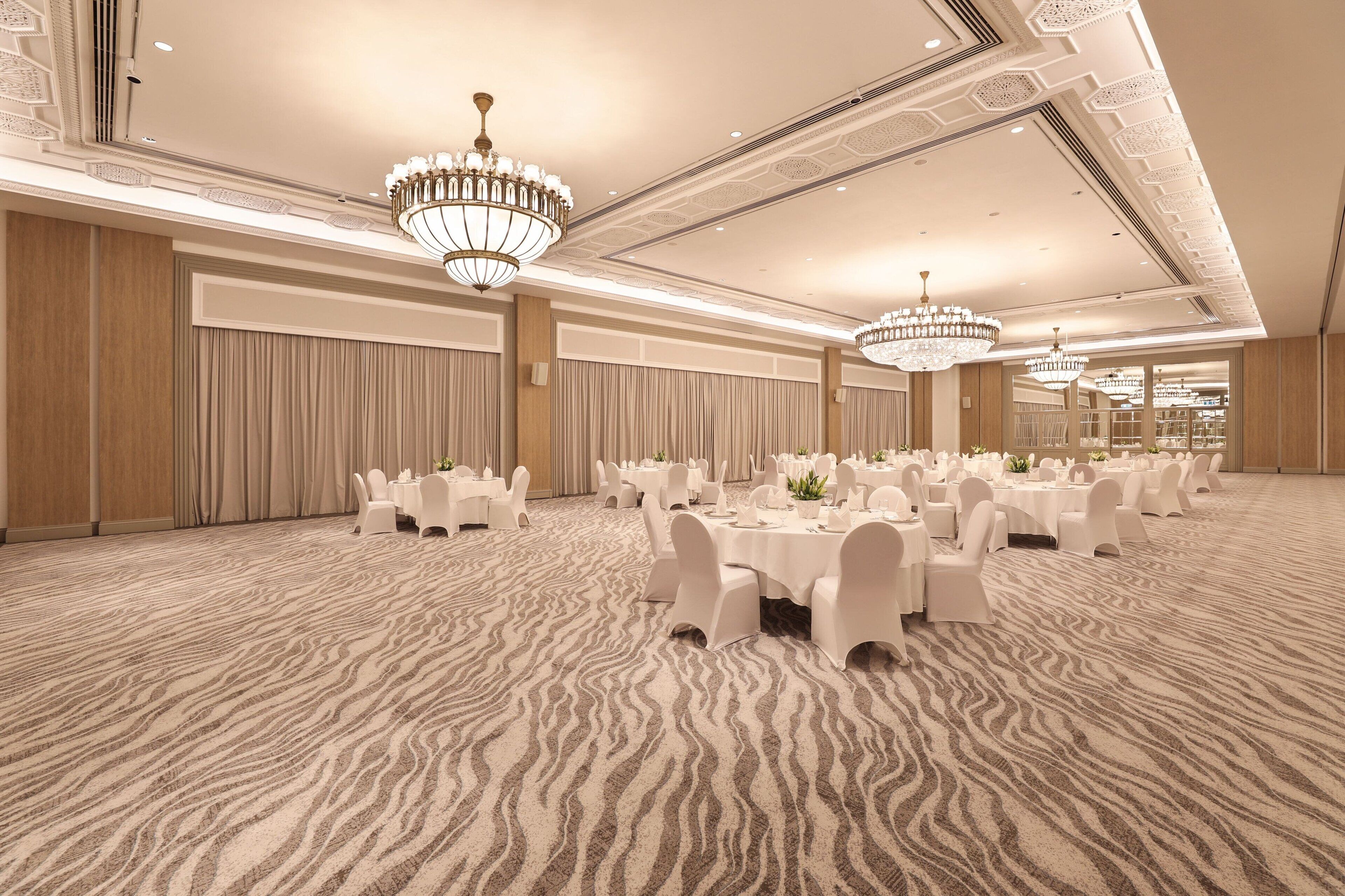 A banquet hall with round tables, white chairs, and chandeliers.