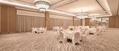 A banquet hall with round tables, white chairs, and chandeliers.