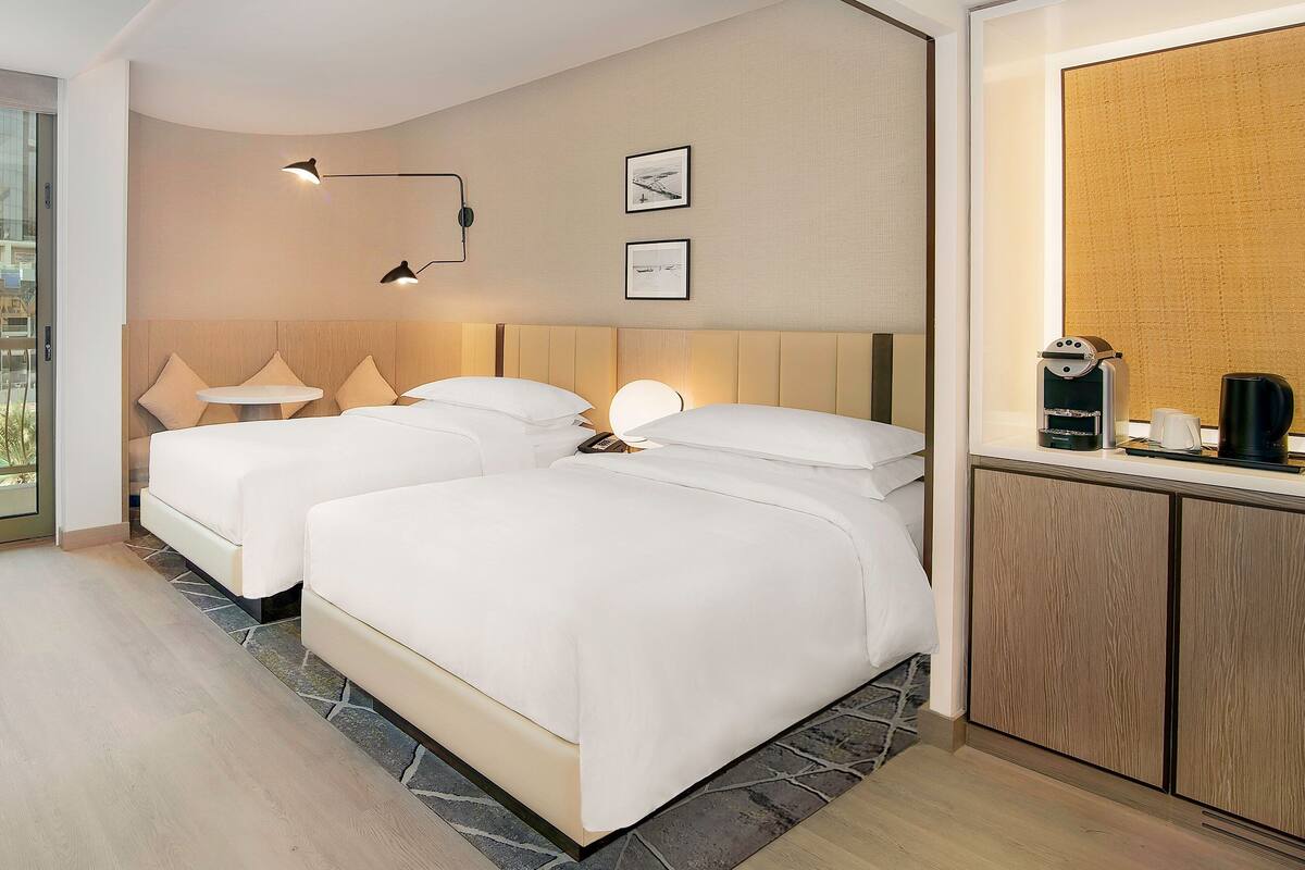 Habitación de hotel con dos camas, una mesita, una cafetera y vistas al exterior.