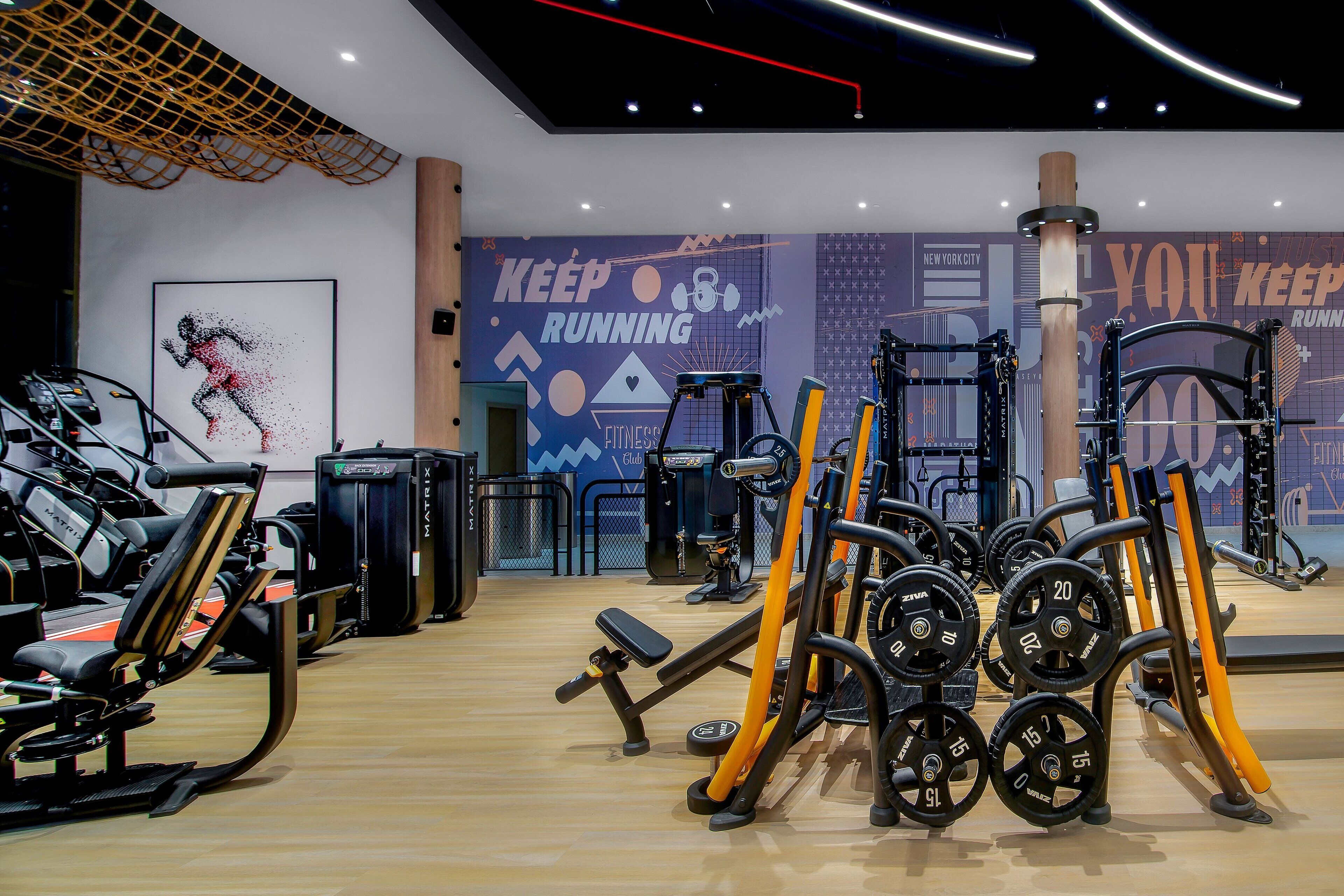 Un gimnasio con diverso equipo de ejercicio, incluyendo cintas de correr, máquinas de pesas y pesas sueltas.