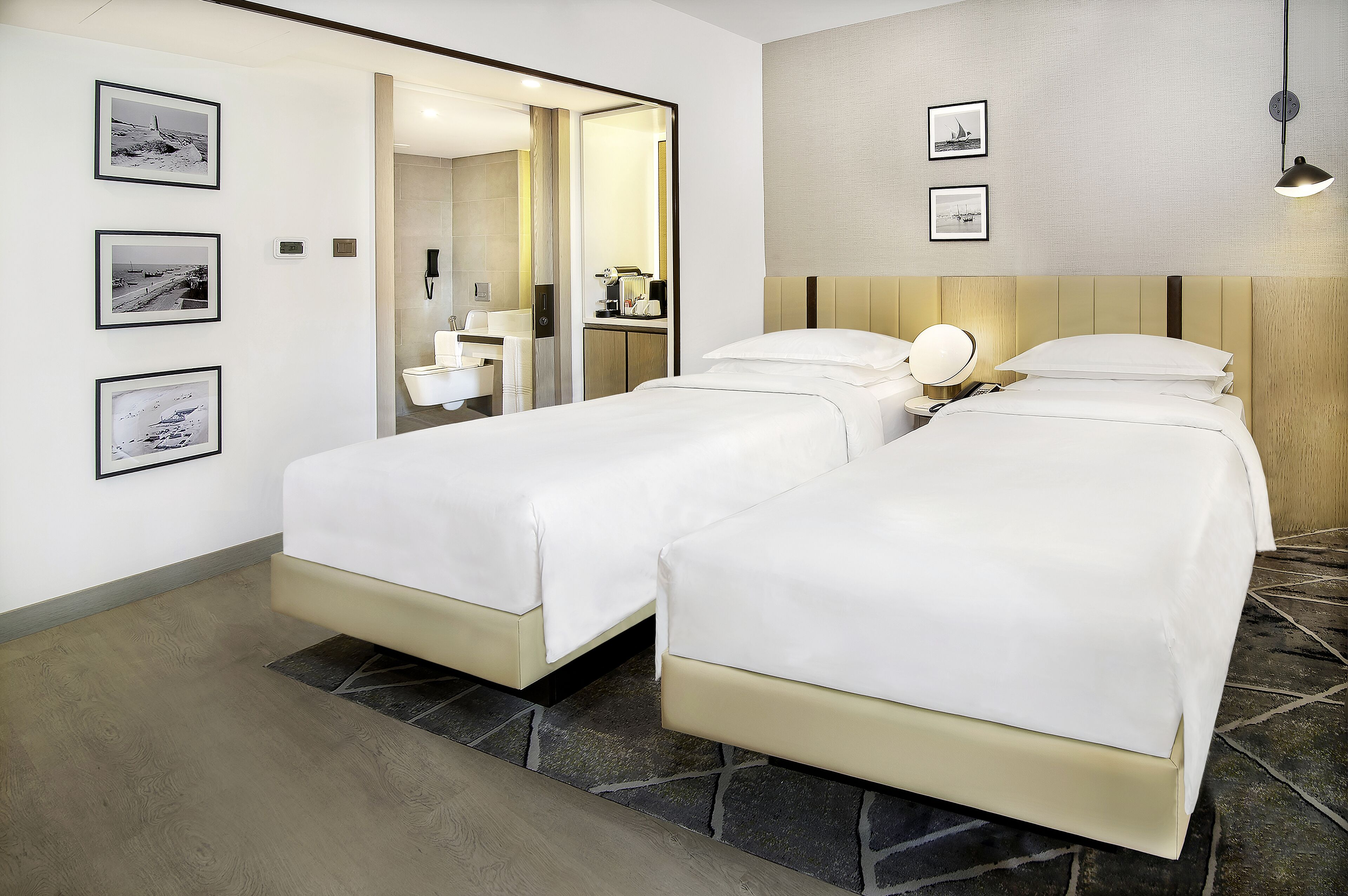A hotel room with two beds, a bathroom with a mirror, and framed pictures on the wall.