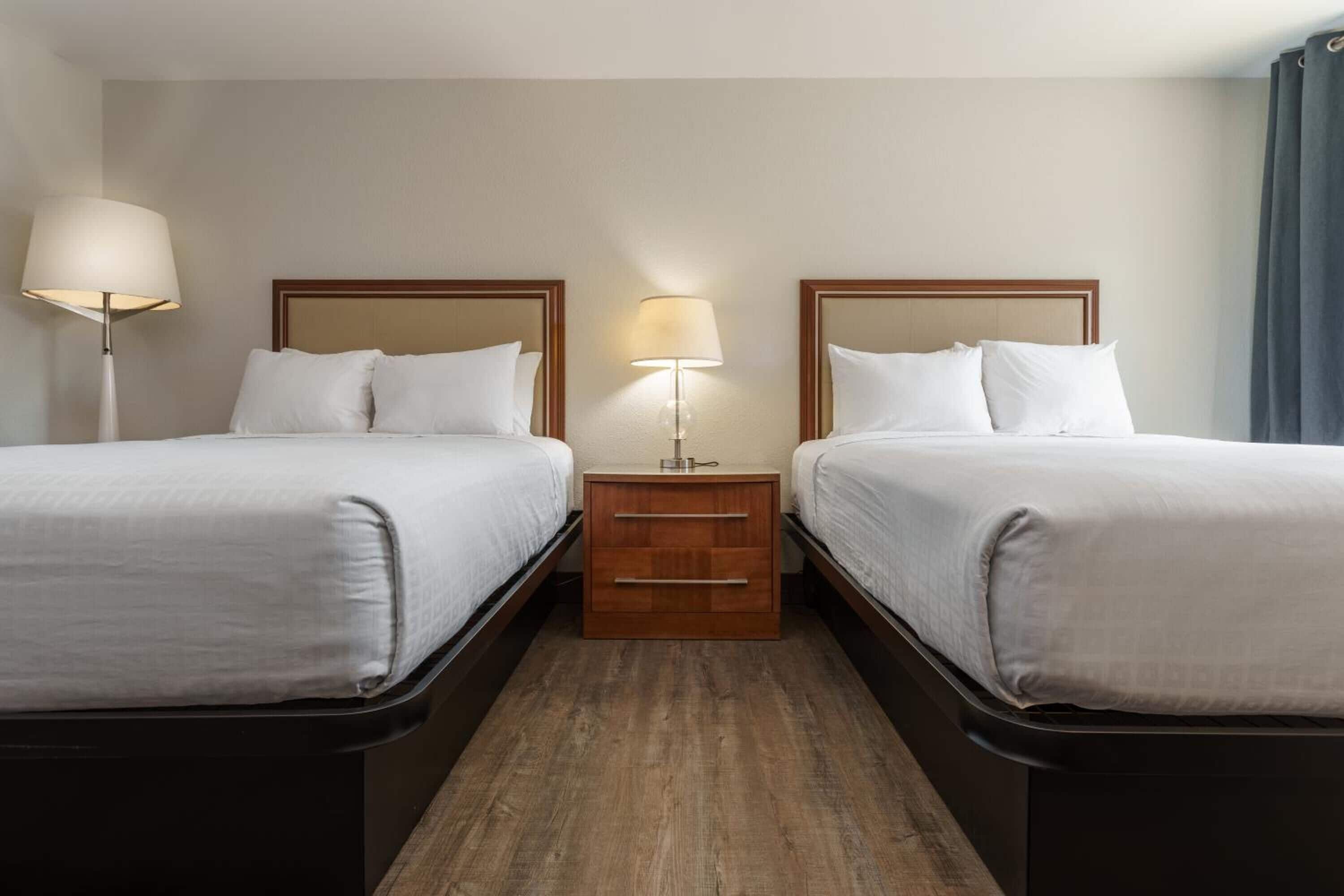A hotel room with two single beds, a bedside table with a lamp, and a small wooden dresser.