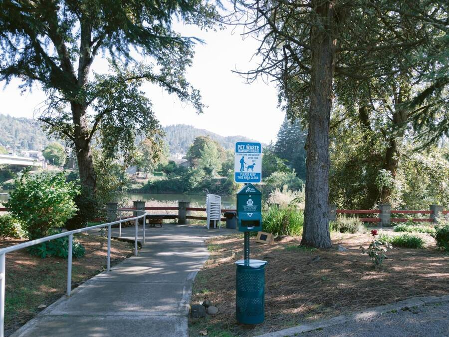 A park pathway with a pet waste station and a sign indicating pet waste disposal.