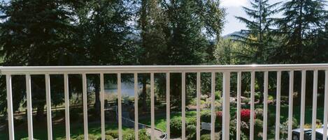 A view from a balcony with a railing, overlooking a parking area and a landscaped garden with various plants and trees.