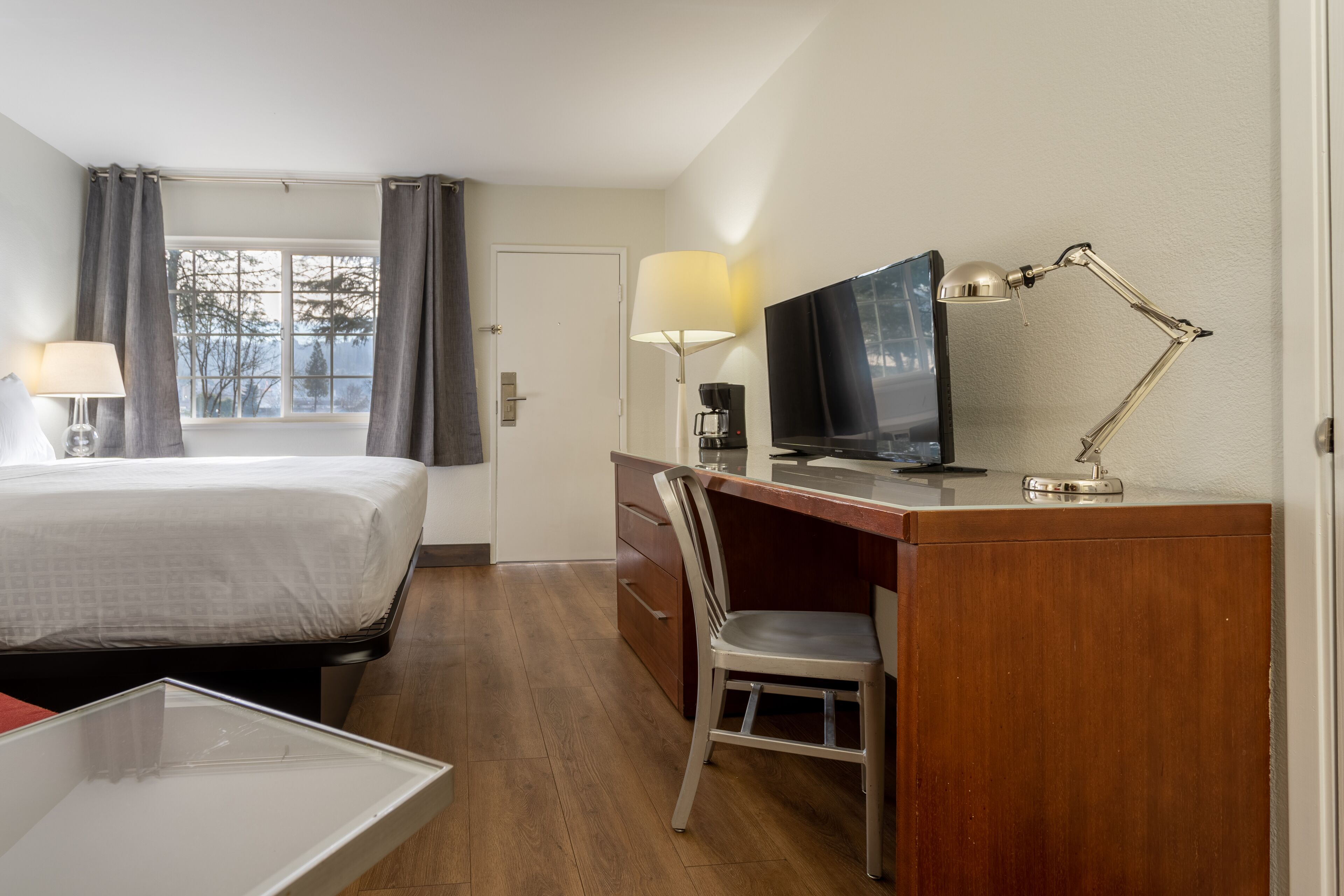 A hotel room with a bed, desk, chair, TV, lamp, and a window with curtains.