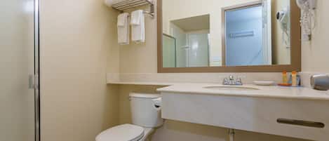 A bathroom with a toilet, sink, and mirror. There are towels on a rack and a hairdryer on the wall.