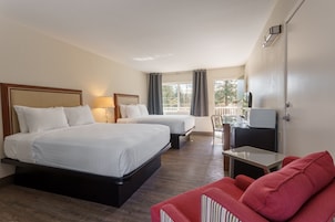 Quarto de hotel com duas camas, uma escrivaninha, uma cadeira e uma televisão.