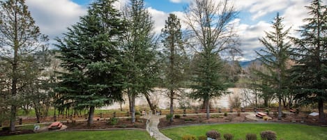 A parking lot with a paved walkway leading to a lake, surrounded by evergreen trees and a grassy area with benches.