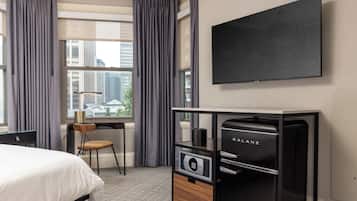 A hotel room with a bed, a desk, a chair, a minibar, and a TV mounted on the wall.