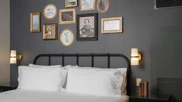 Una cama bien hecha con sábanas blancas, cabecera de metal negro y dos lámparas de lectura fijadas a la pared.