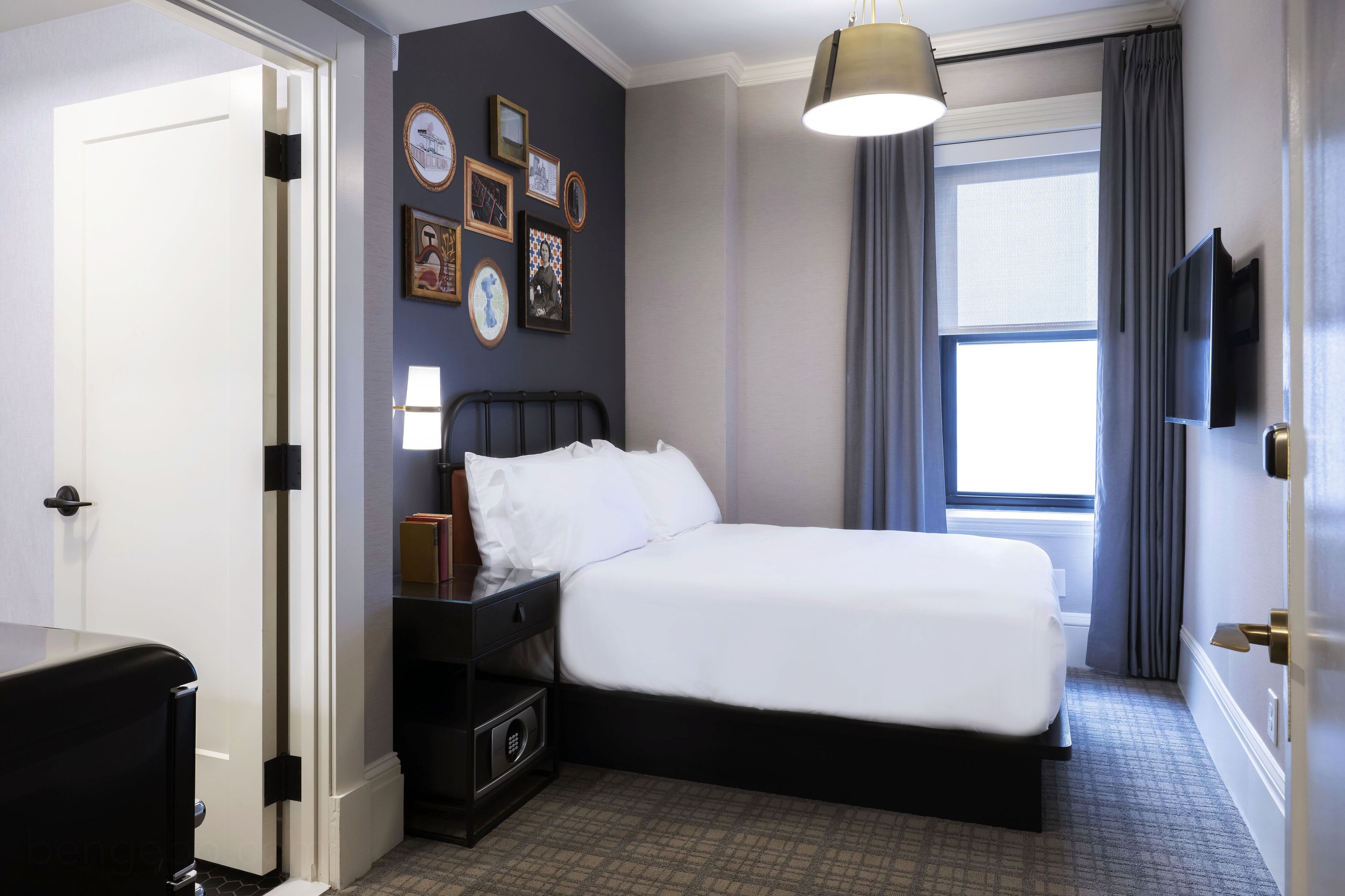 A hotel room with a bed, bedside table, lamp, and wall-mounted TV.