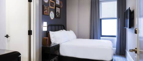 A hotel room with a bed, bedside table, lamp, and wall-mounted TV.