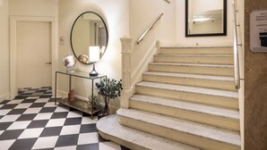 A checkered floor, a staircase with a handrail, a round mirror, and a small table with a globe. - Copley Square Hotel, a FOUND Hotel (Boston)