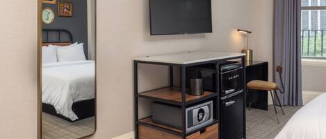 Ett hotellrum med en säng, en tv, ett skrivbord med en lampa, en stol och ett fönster med gardiner.
