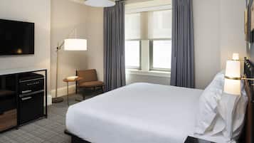 A hotel room with a large bed, a desk with a flat-screen TV, a lamp, and a chair.