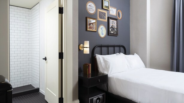 A hotel room with a bed, a nightstand, a wall-mounted lamp, and a door leading to a bathroom. - Copley Square Hotel, a FOUND Hotel (Boston)