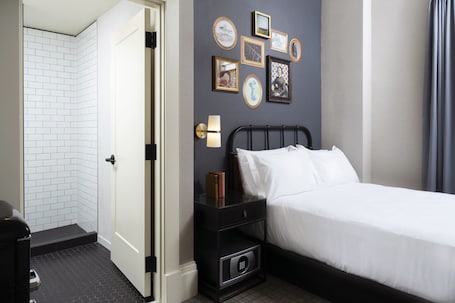 A hotel room with a bed, a nightstand, a wall-mounted lamp, and a door leading to a bathroom.